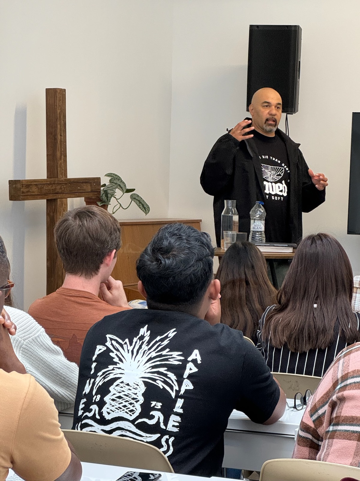 A speaker teaching a seated group beside a wooden cross